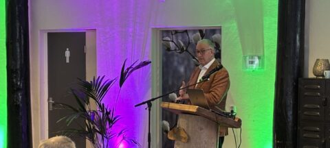 Man geeft presentatie aan publiek in verlichte ruimte met groene planten.