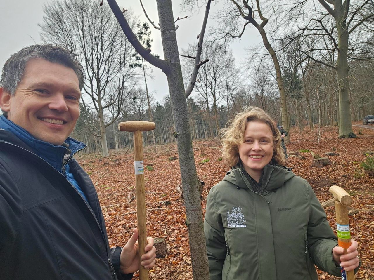 Twee mensen poseren met spades in een winters bos, klaar voor boomplantactiviteiten.