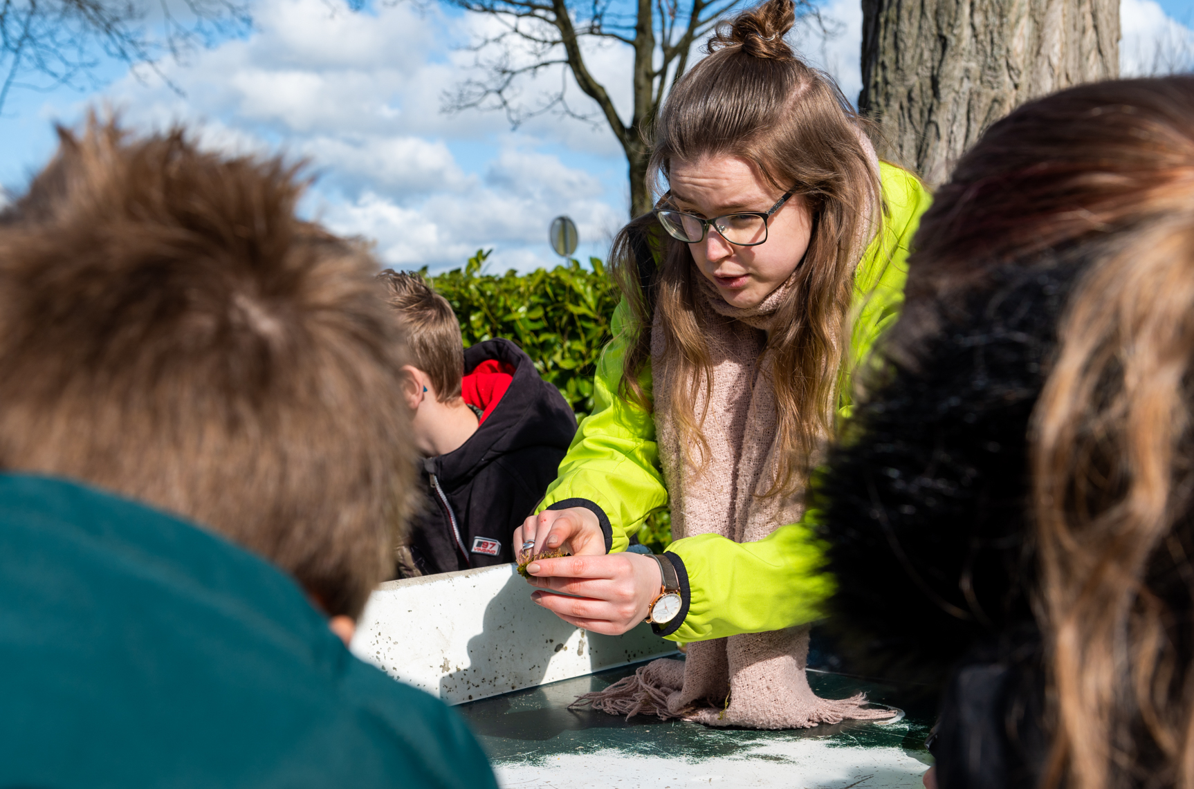Een vrouw in een gele jas toont iets aan kinderen buiten.