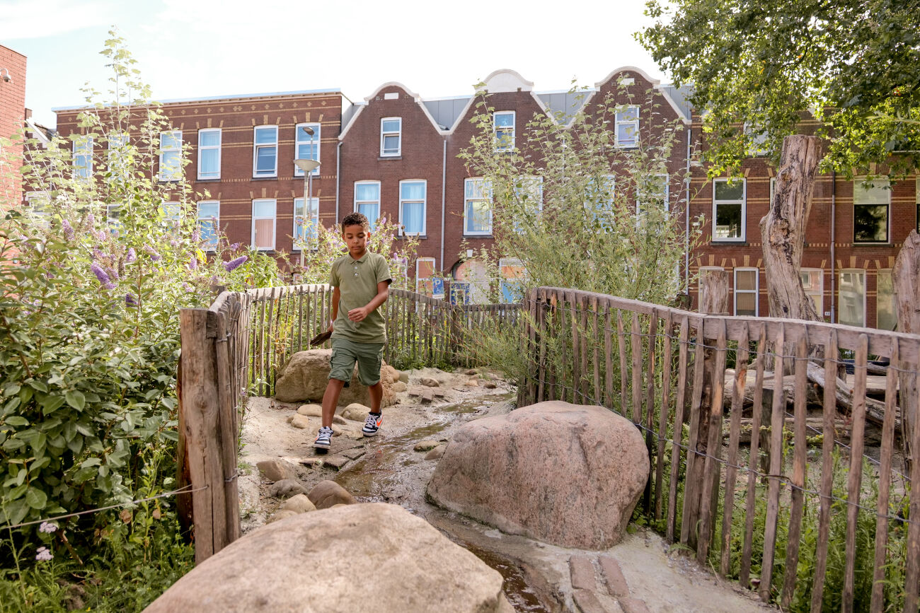 Jongen loopt over een pad met stenen in een groene stadstuin voor rijhuizen.