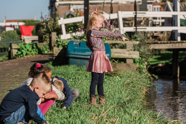 Kinderen spelen aan de waterkant naast een brug op een zonnige dag.