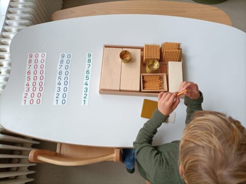 Kind gebruikt Montessori-materiaal met kralen en nummers op tafel voor rekenles.
