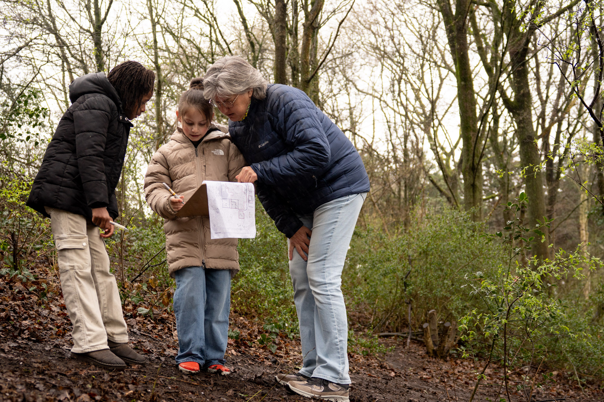 Drie personen bekijken een kaart in een bosrijke omgeving.