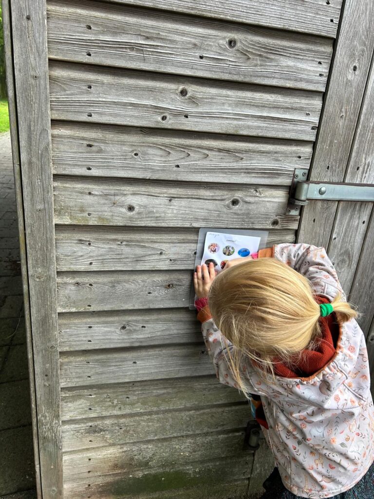 Kind plakt een vel papier op een houten schuurmuur.