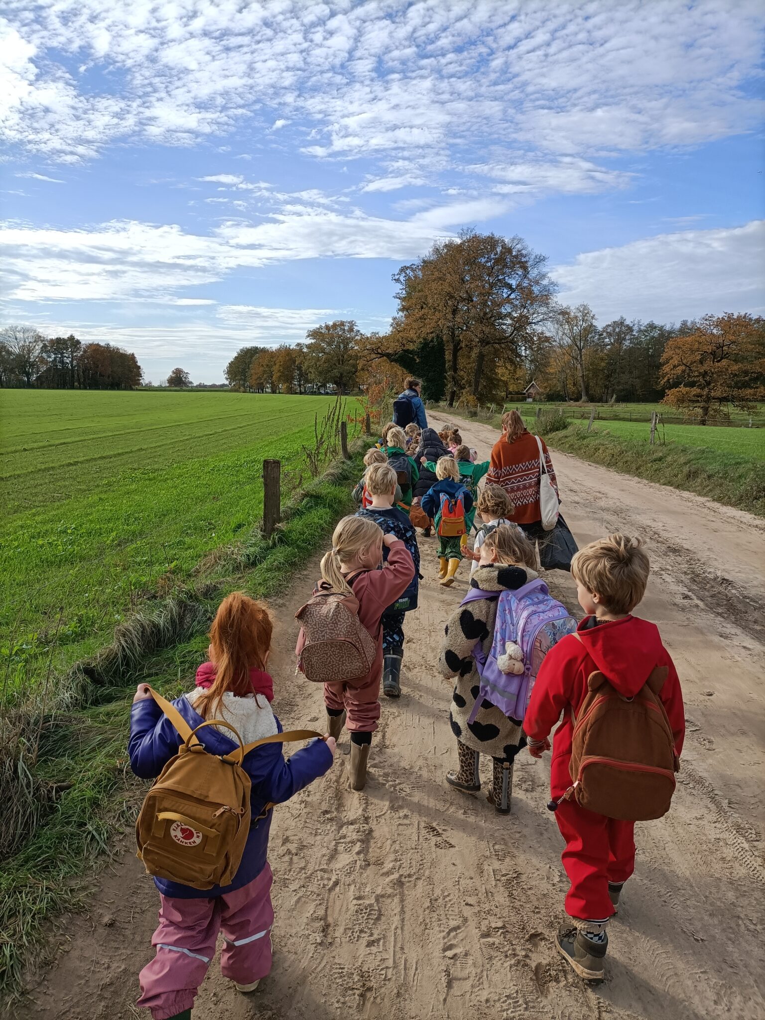 Kinderen wandelen op een zandpad langs een groene weide onder een bewolkte hemel.