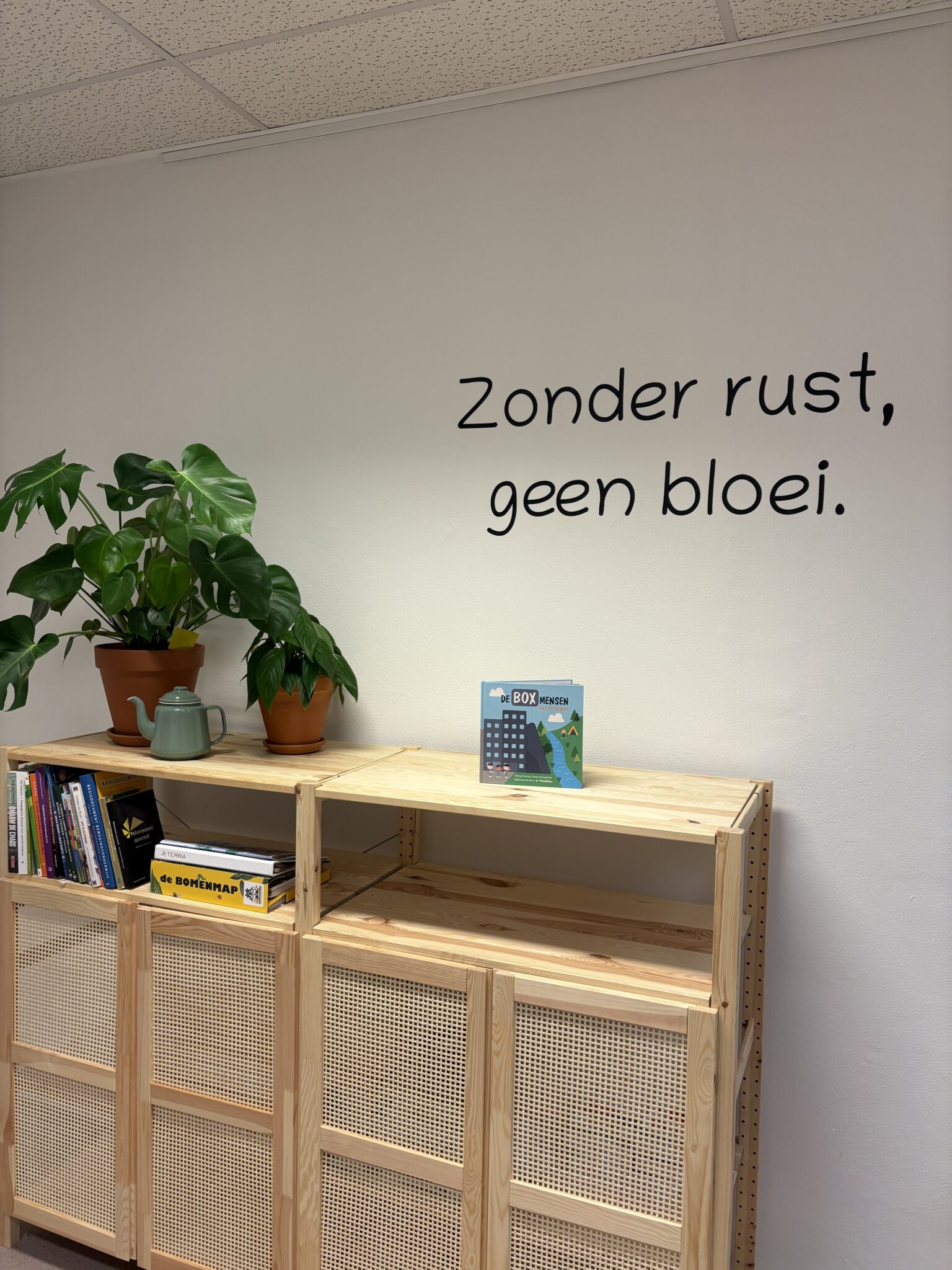 Plank met planten en boeken, tekst op muur: "Zonder rust, geen bloei."