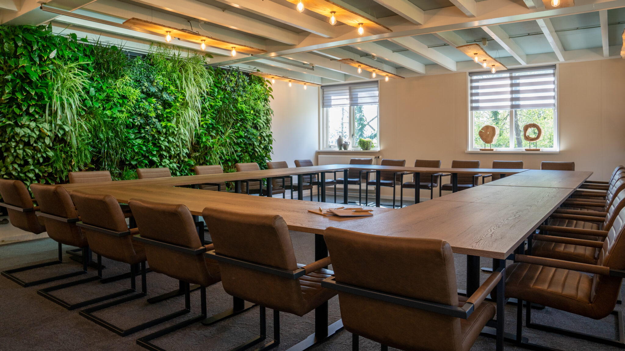 Vergaderruimte met U-vormige tafel, leren stoelen, verticale plantenwand en grote ramen.