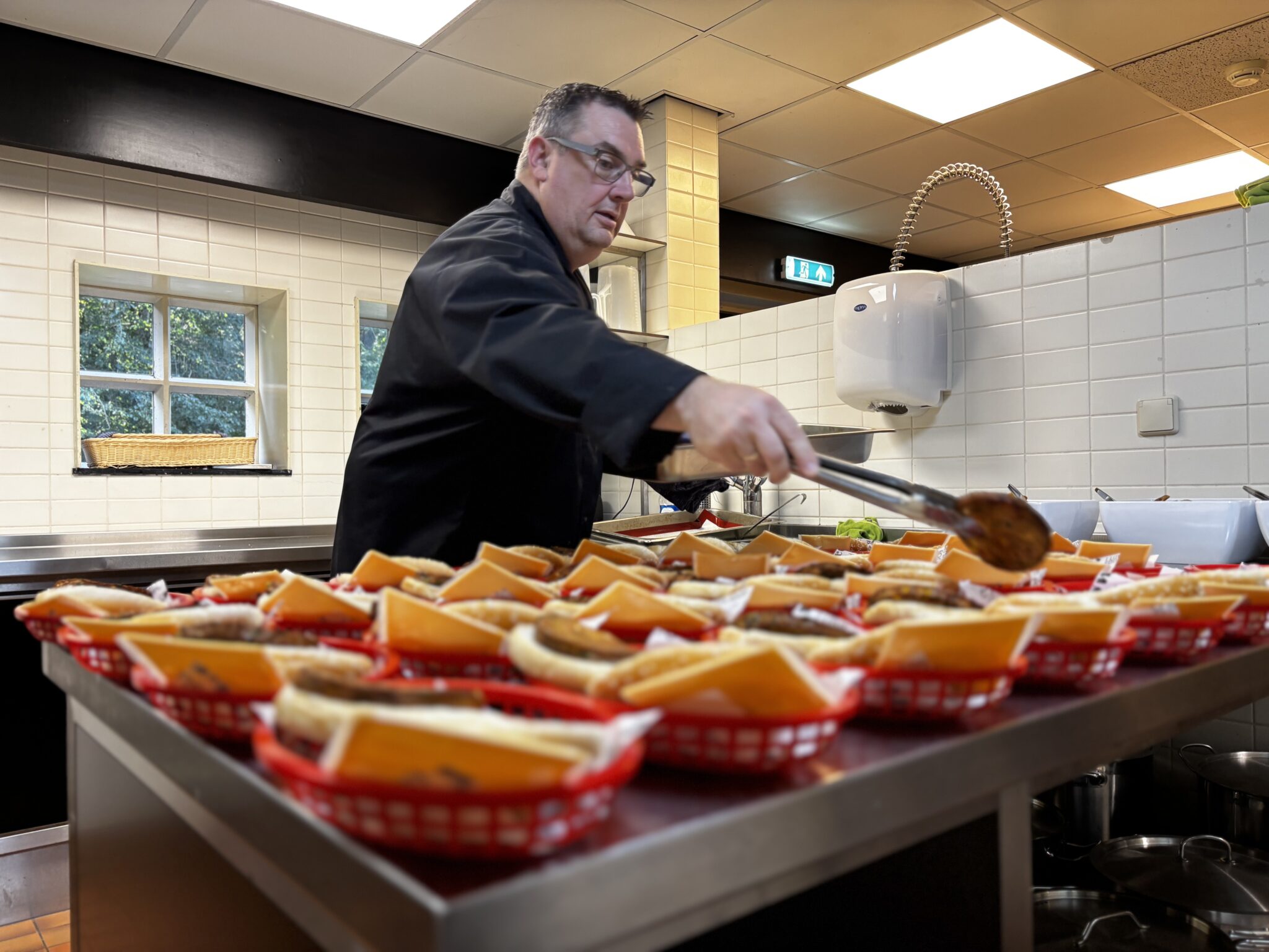 Man in keuken serveert broodjes in rode mandjes op een roestvrijstalen aanrecht.