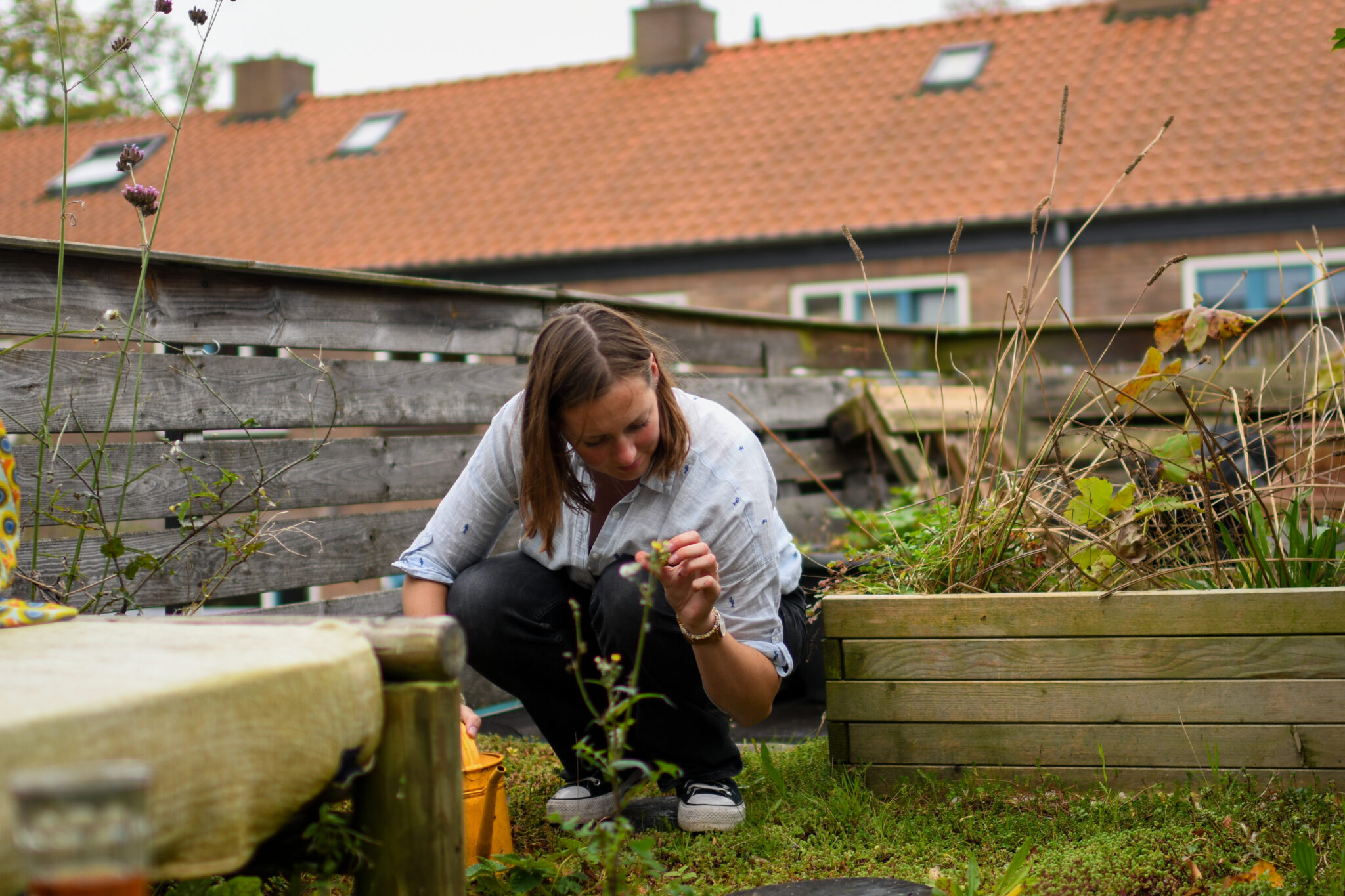 Vrouw tuiniert in een kleine, groene achtertuin met houten rek en plantenbakken.