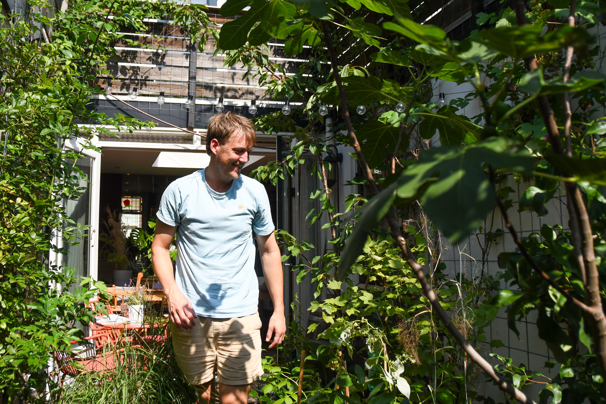 Man wandelt door een groene, weelderige tuin voor een modern huis met glazen deuren.