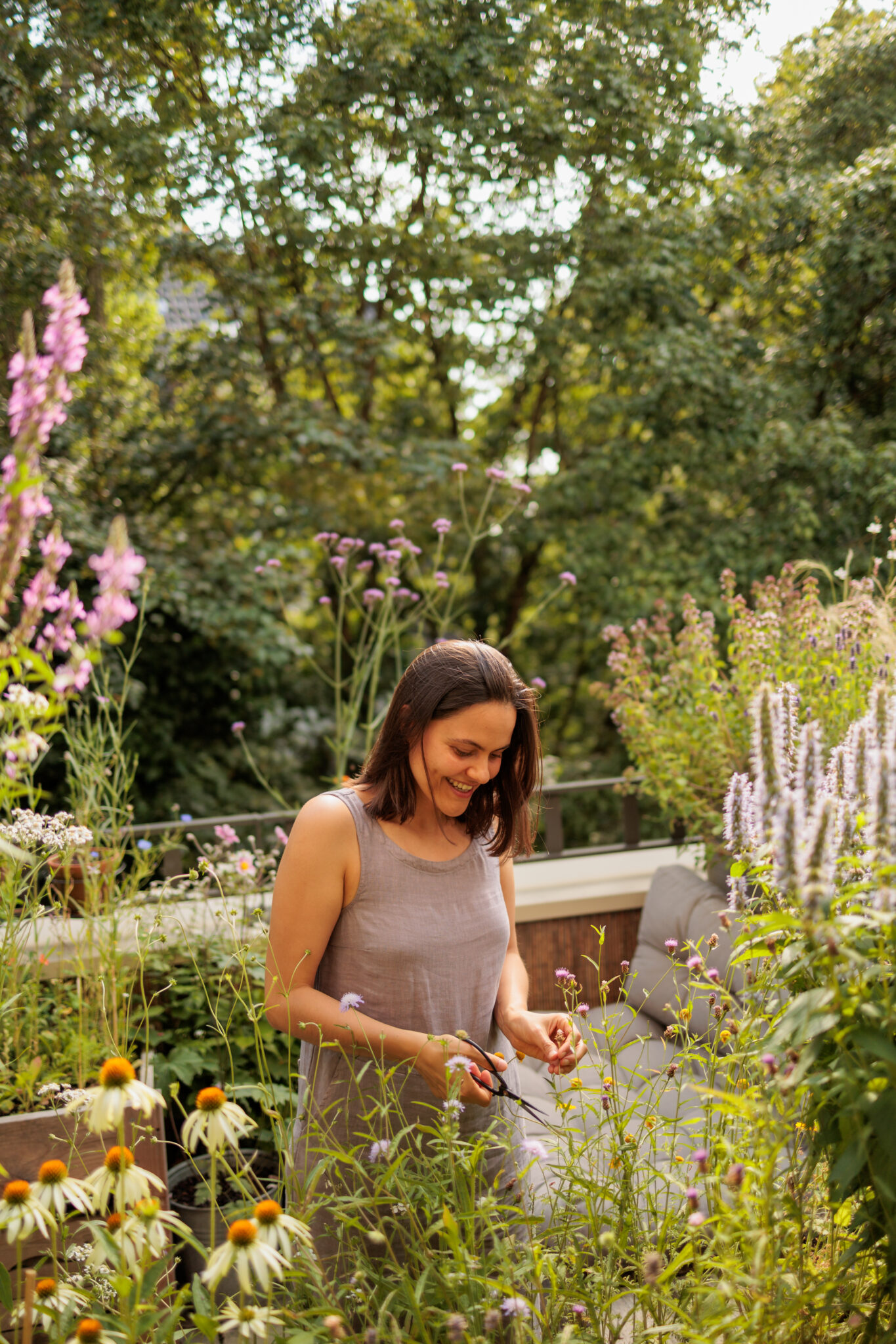 Vrouw in een tuin met bloemen, genietend van het groene uitzicht en lachend.
