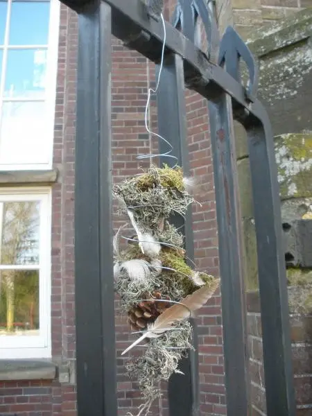 Takken en mos hangen aan een draad aan een zwart metalen hek voor een bakstenen gebouw.