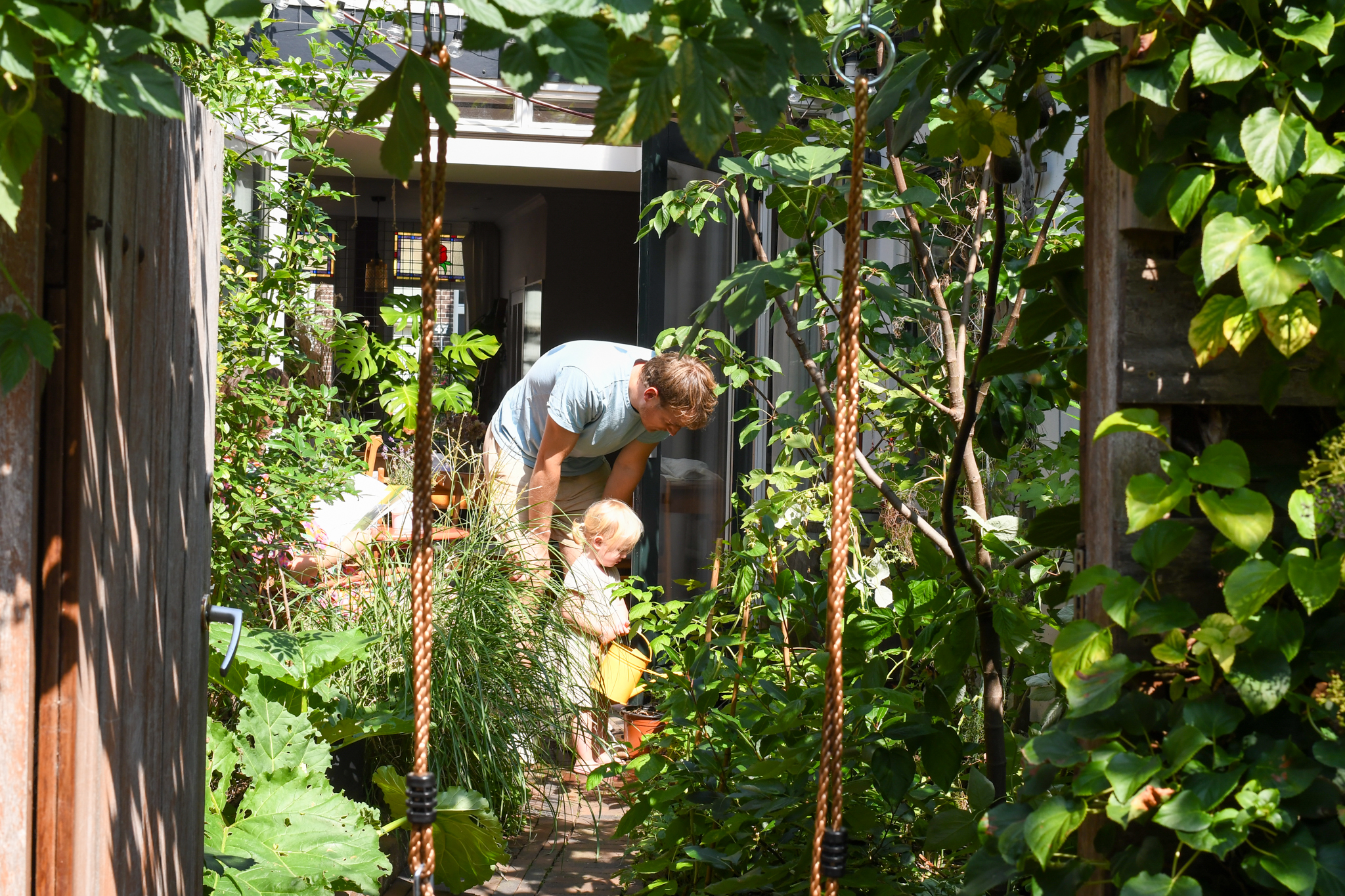 Man en kind in groene tuin, kind met gieter, heldere zomerdag.