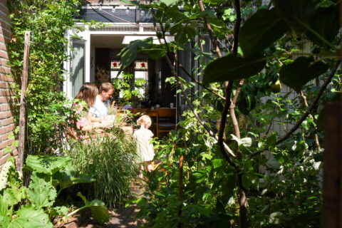 Gezin geniet van zonnige dag in weelderige tuin, omgeven door groene planten en bomen.