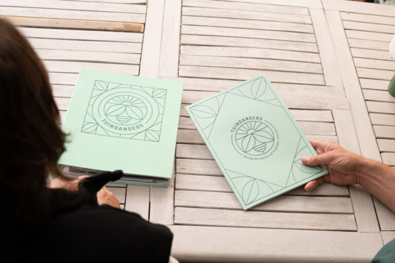 Twee mensen bekijken Tuinrangers-mappen op een houten tafel.