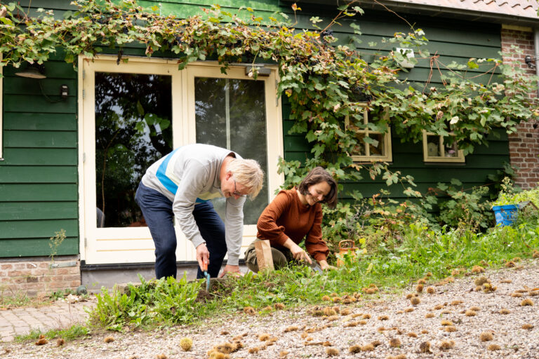 Twee mensen onkruid wieden voor een groen huis met druivenranken.