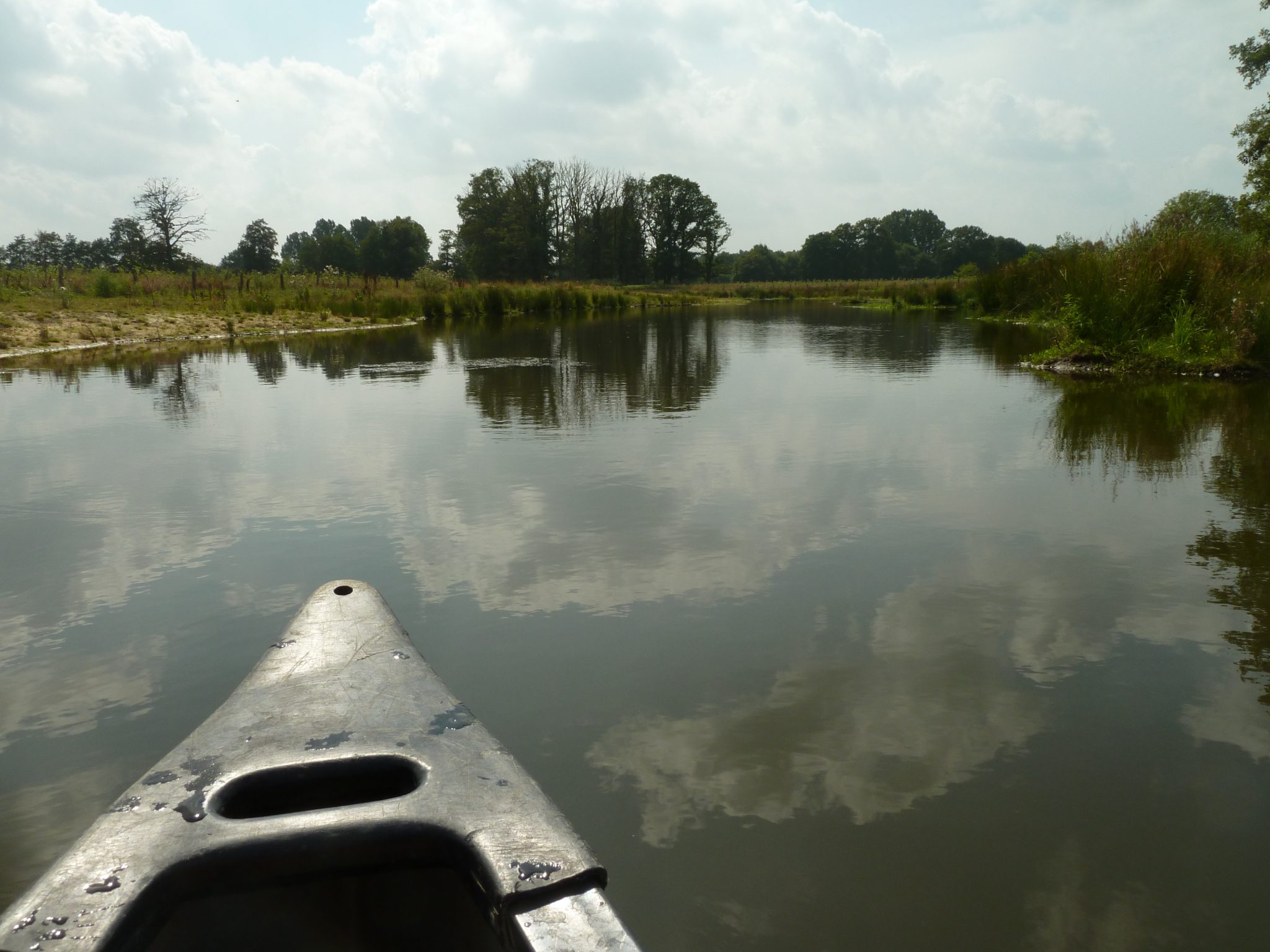 Kano op een rustige rivier met bomen en bewolkte lucht weerspiegeld in het water.