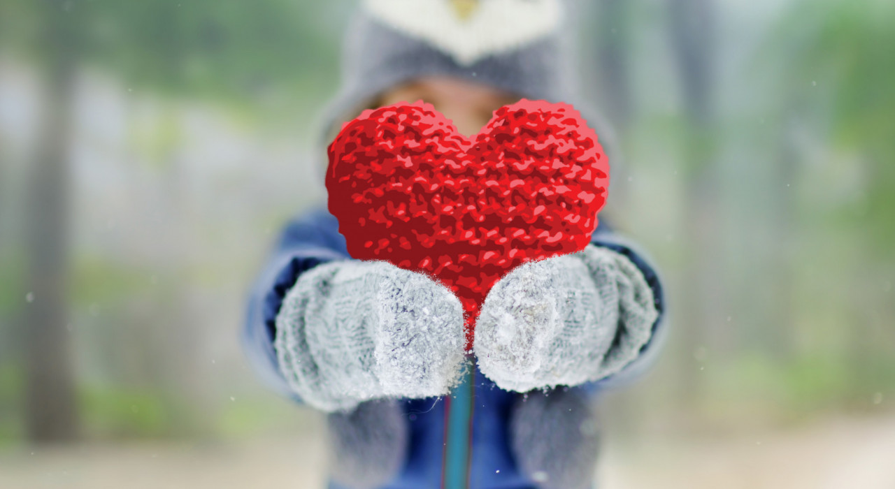 Kind in winterkleding houdt een groot, rood hart vast in beide handen.