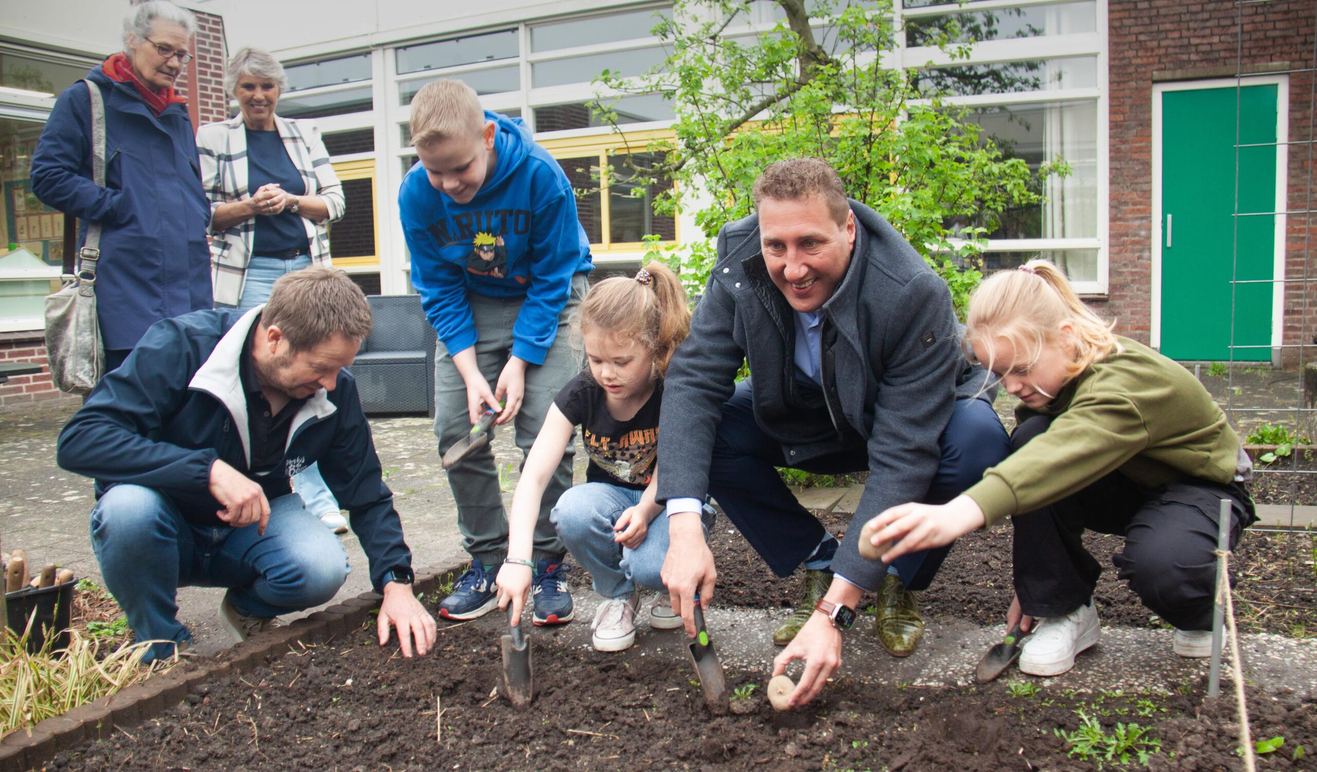 Groep mensen plant zaden in een tuin, met kinderen en volwassenen die samenwerken.