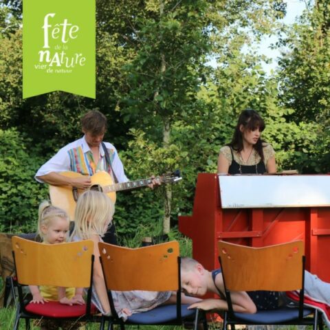 Muzikanten spelen buiten, kinderen zitten op stoelen. Tekst: "Fête de la Nature, vier de natuur".