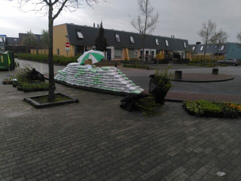 Stapel zandzakken met paraplu naast planten in woonwijk.