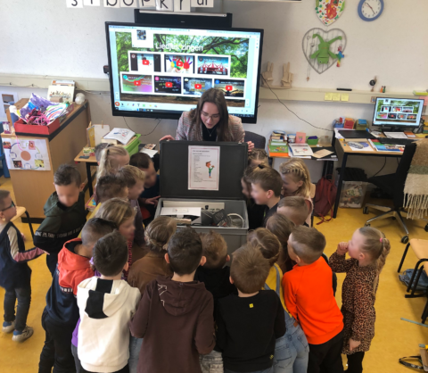 Een groep kinderen verzameld rond een open koffer in een klaslokaal.