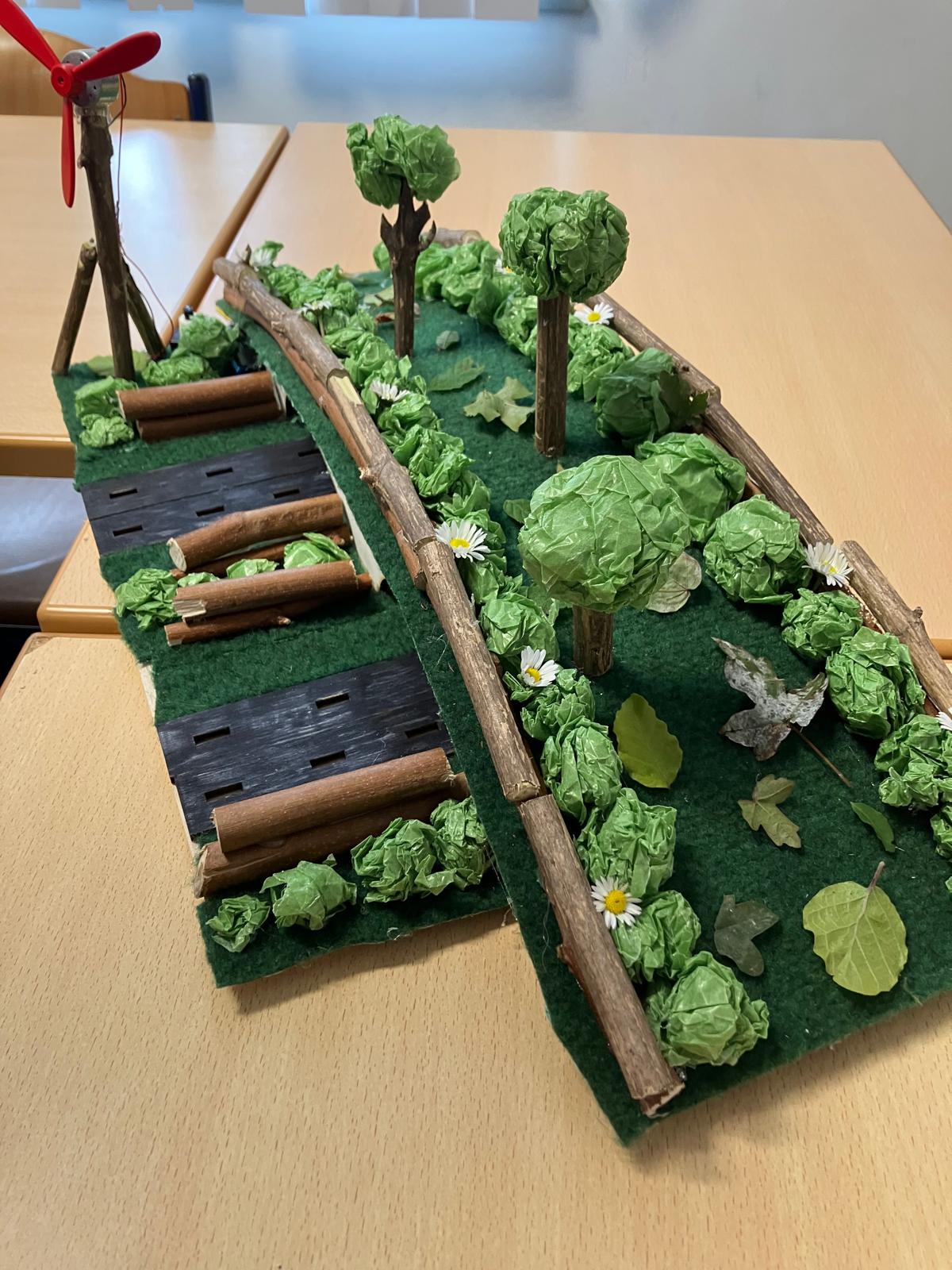 Miniatuurlandschap met bomen, planten en een windmolen op een tafel.