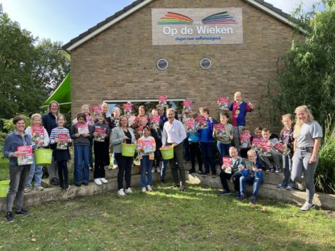 Groep kinderen en volwassenen voor CBS Op de Wieken, met boeken en groene emmers in handen.