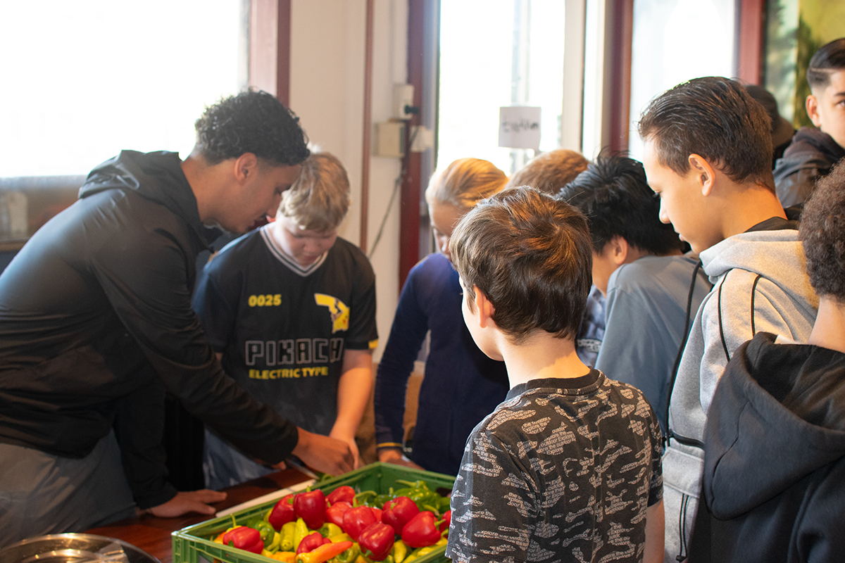 Groep kinderen verzameld rond een tafel met paprika's in een krat.
