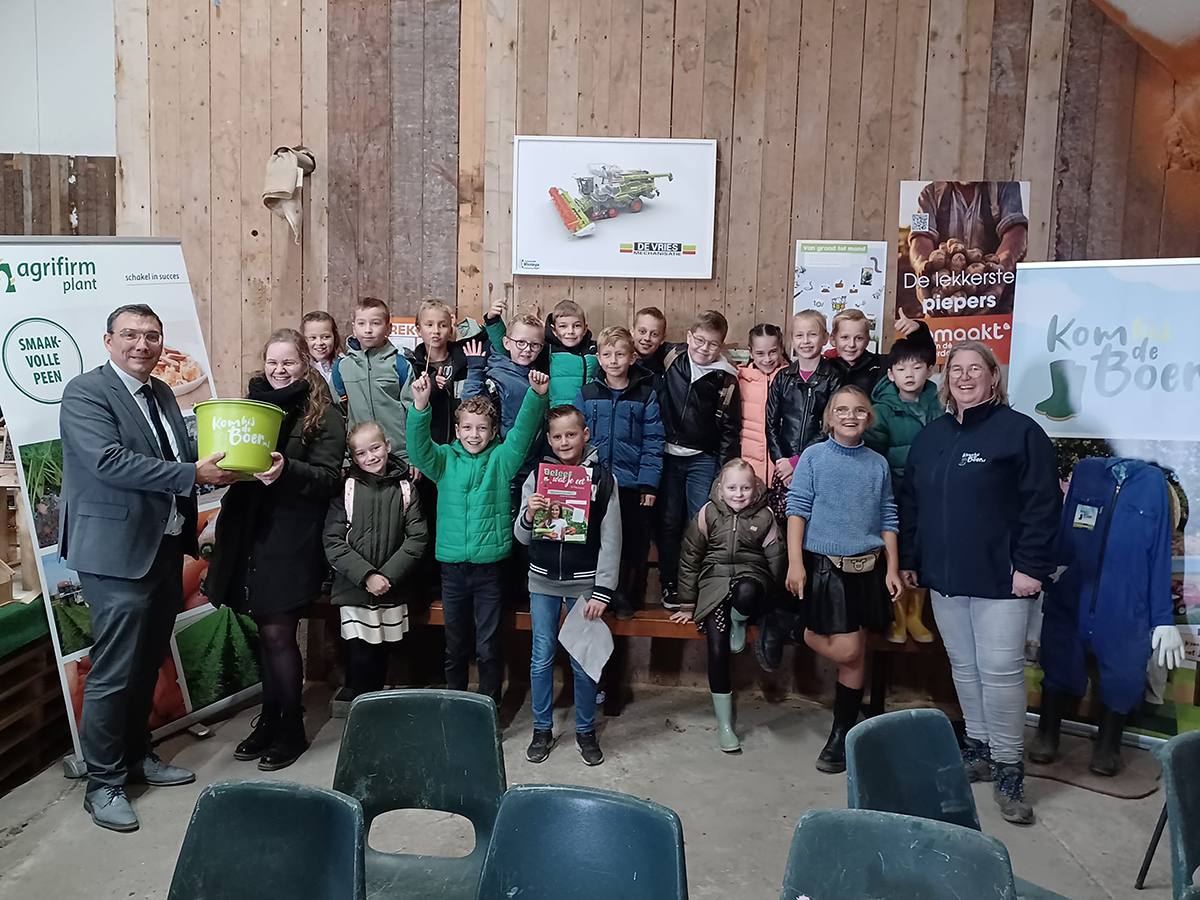 Een groep kinderen en volwassenen poseert in een schuur met boerenposters op de achtergrond.