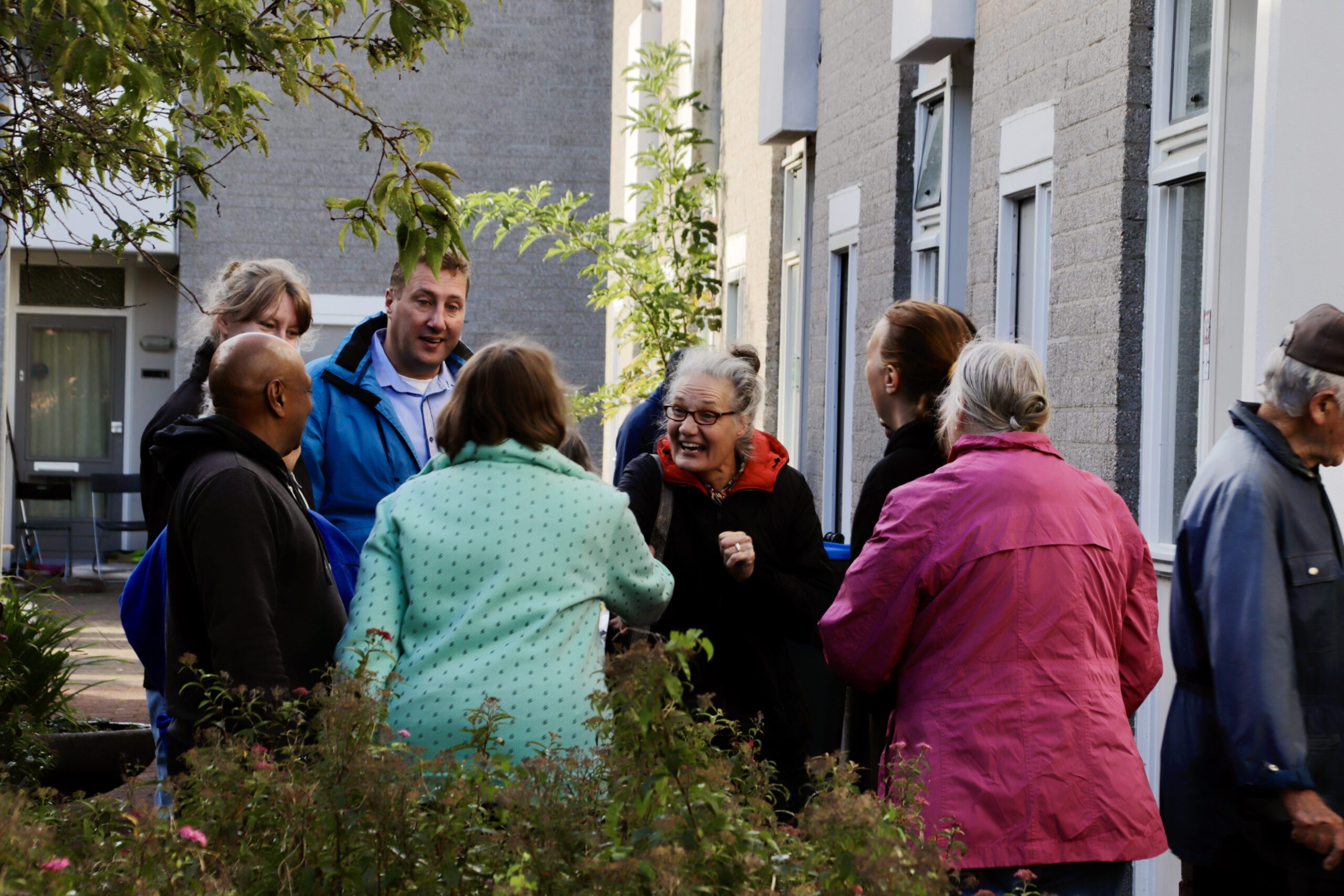 Een groep mensen voert een levendig gesprek voor een rij huizen.