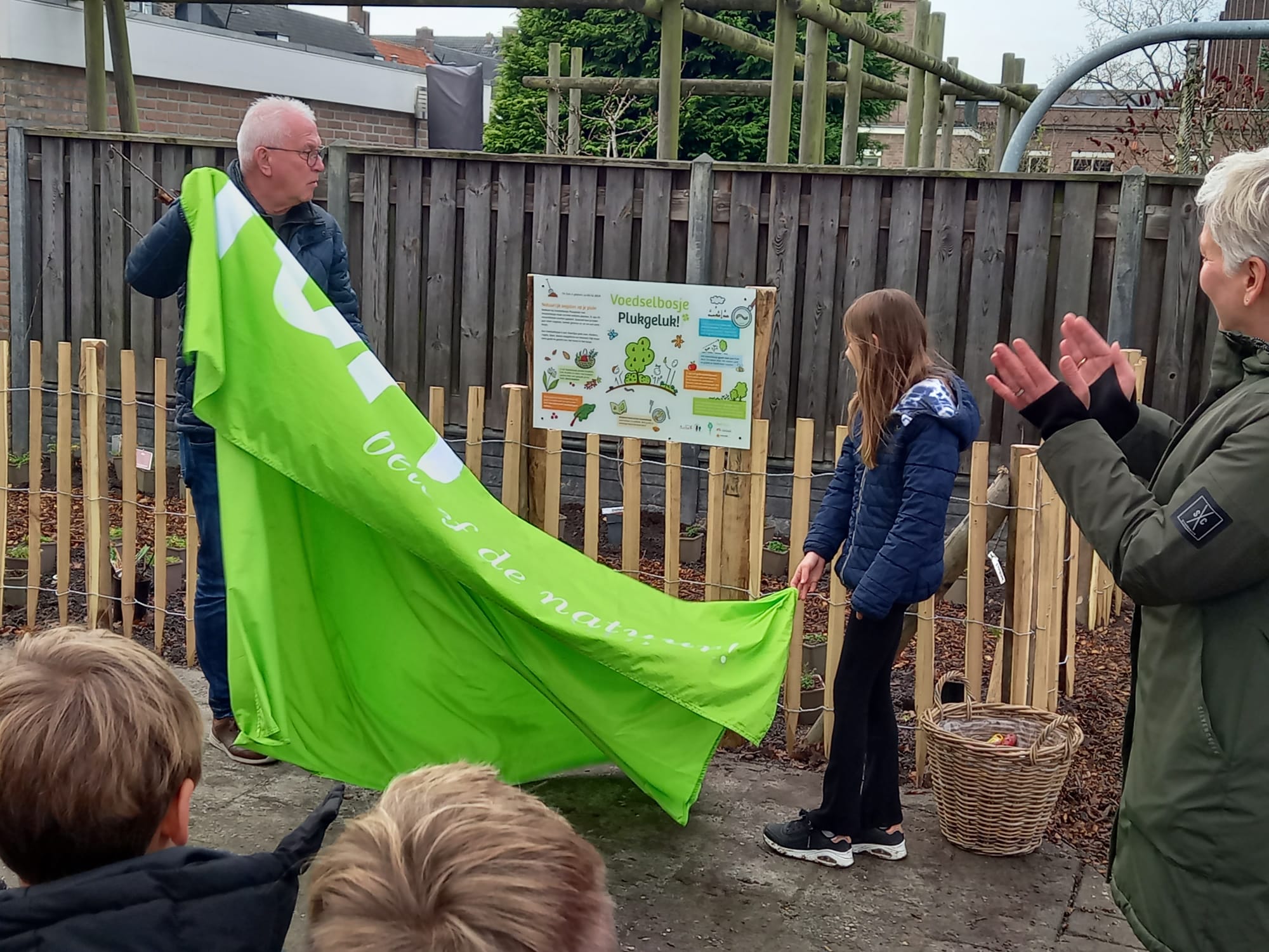 Man en meisje onthullen bord bij omheind gebied, omstanders klappen.