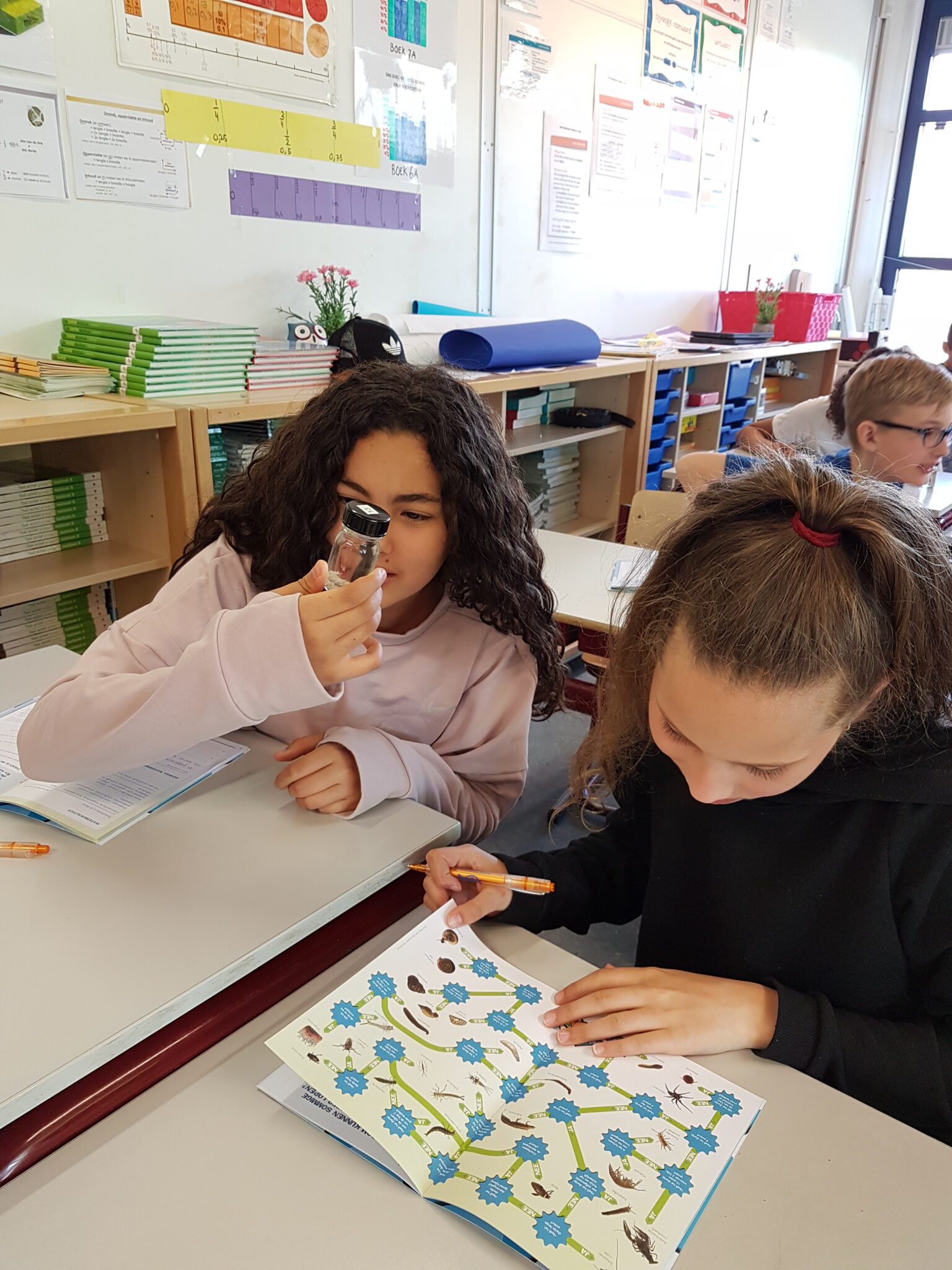 Twee kinderen in klas onderzoeken een boek met een vergrootglas.