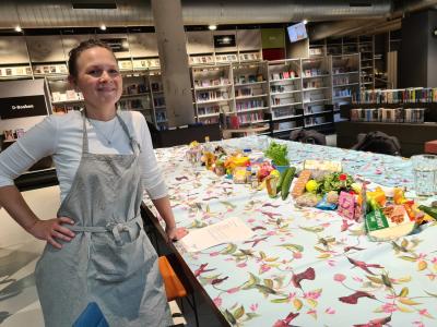 Vrouw in schort bij kleurrijk gedekte tafel met voedsel in winkelomgeving.