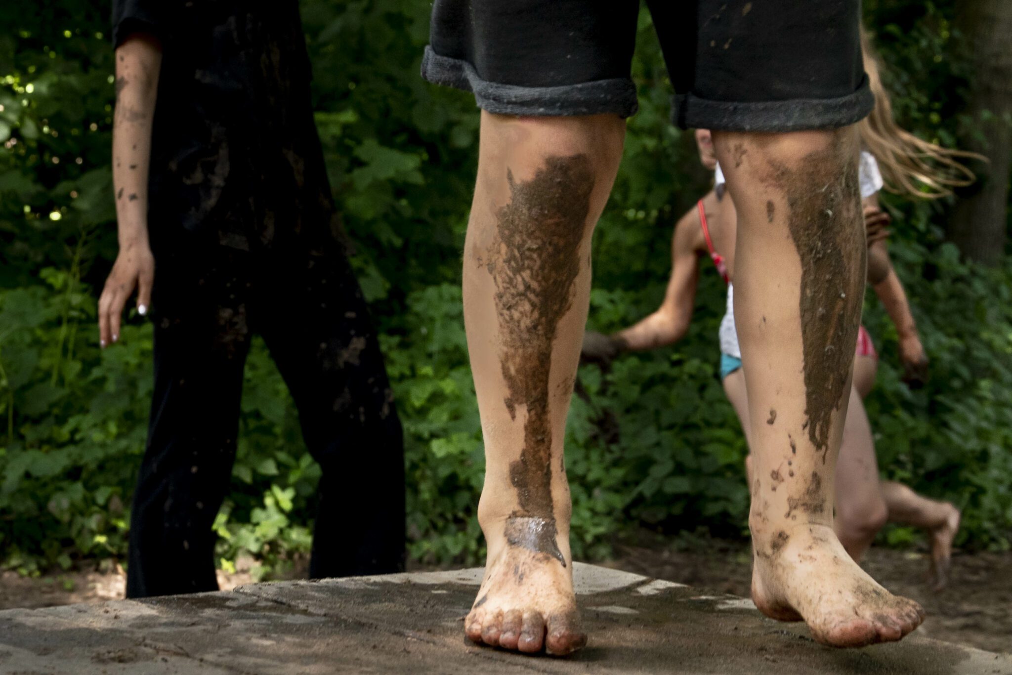 Kinderen met modderige benen spelen buiten op blote voeten in een bosrijke omgeving.