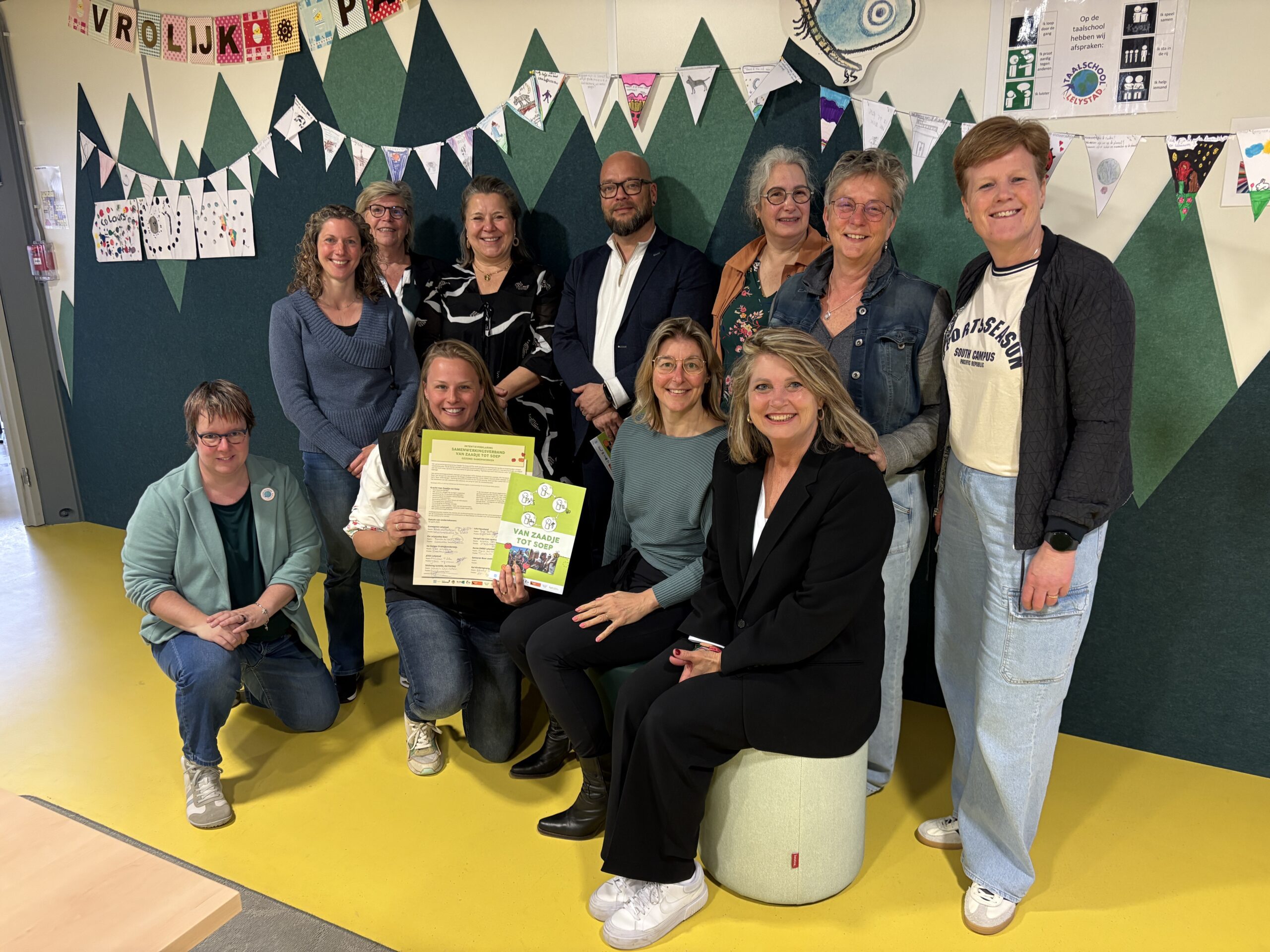 Groep lachende mensen met certificaten poseren voor versierde wand.