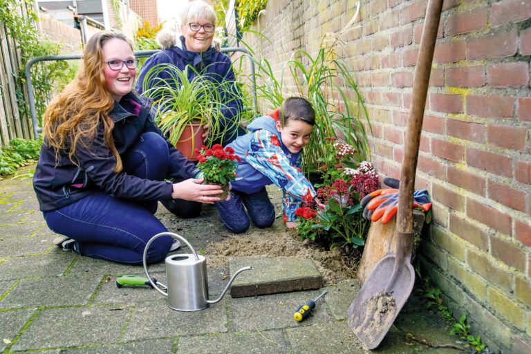 Drie mensen planten bloemen in een tuin met gereedschap en een gieter.