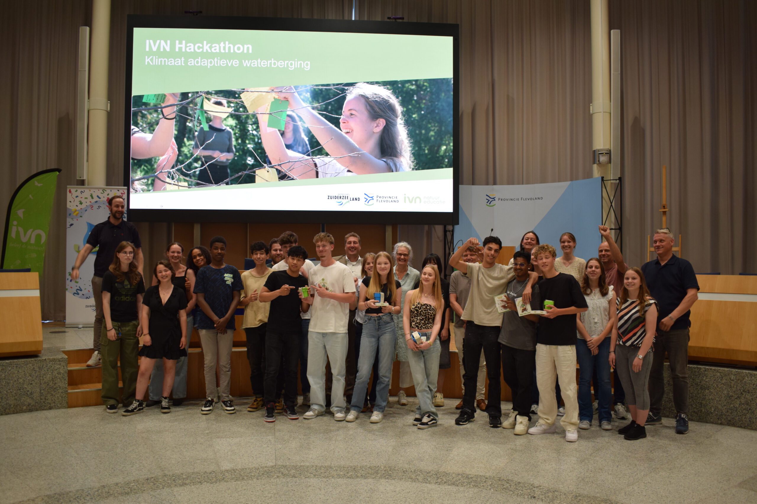 Groep mensen poseert voor een groot scherm met de tekst "IVN Hackathon: Klimaat adaptieve waterberging".