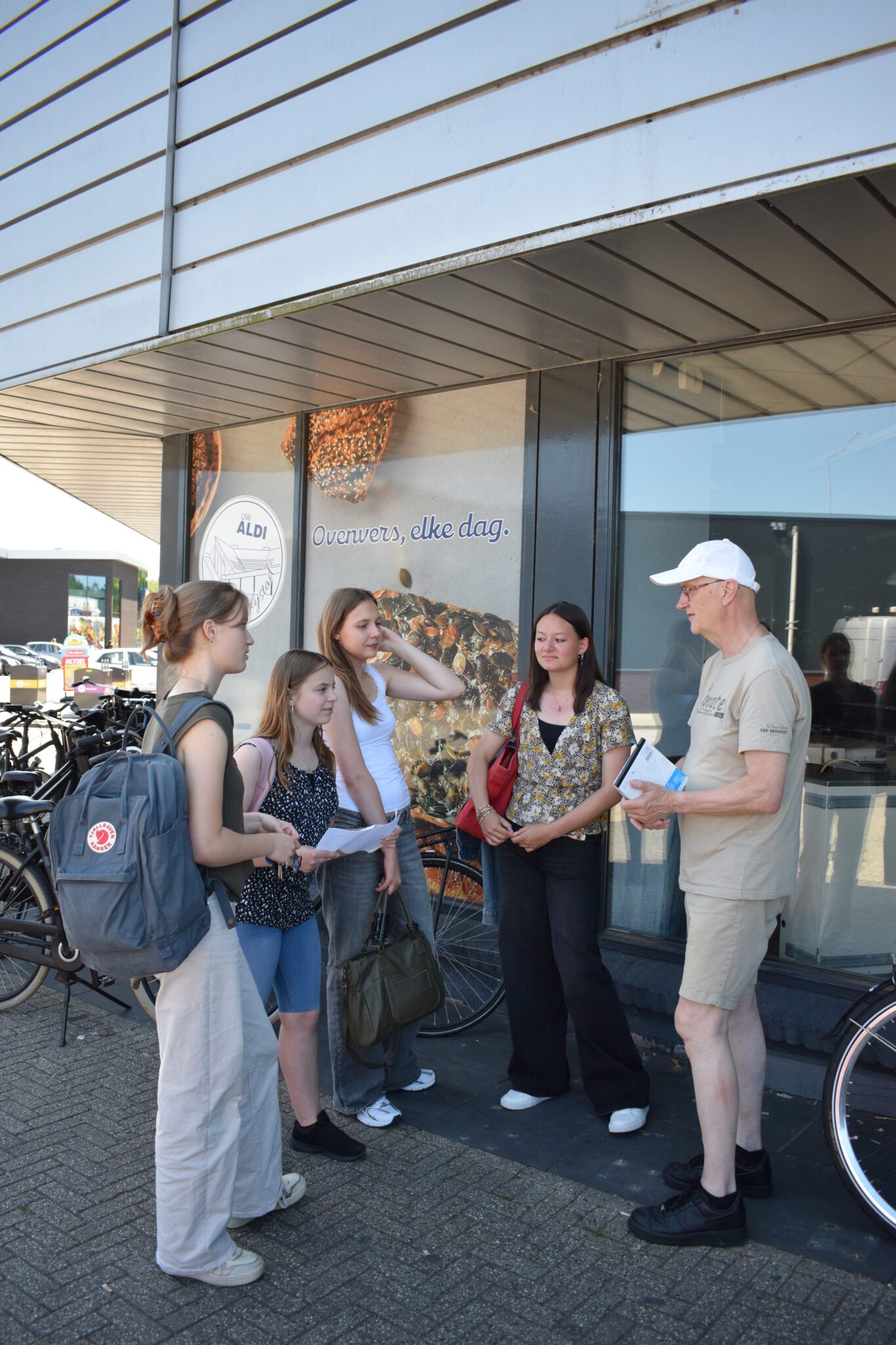 Groep mensen staat buiten een winkel, in gesprek naast fietsenrekken.