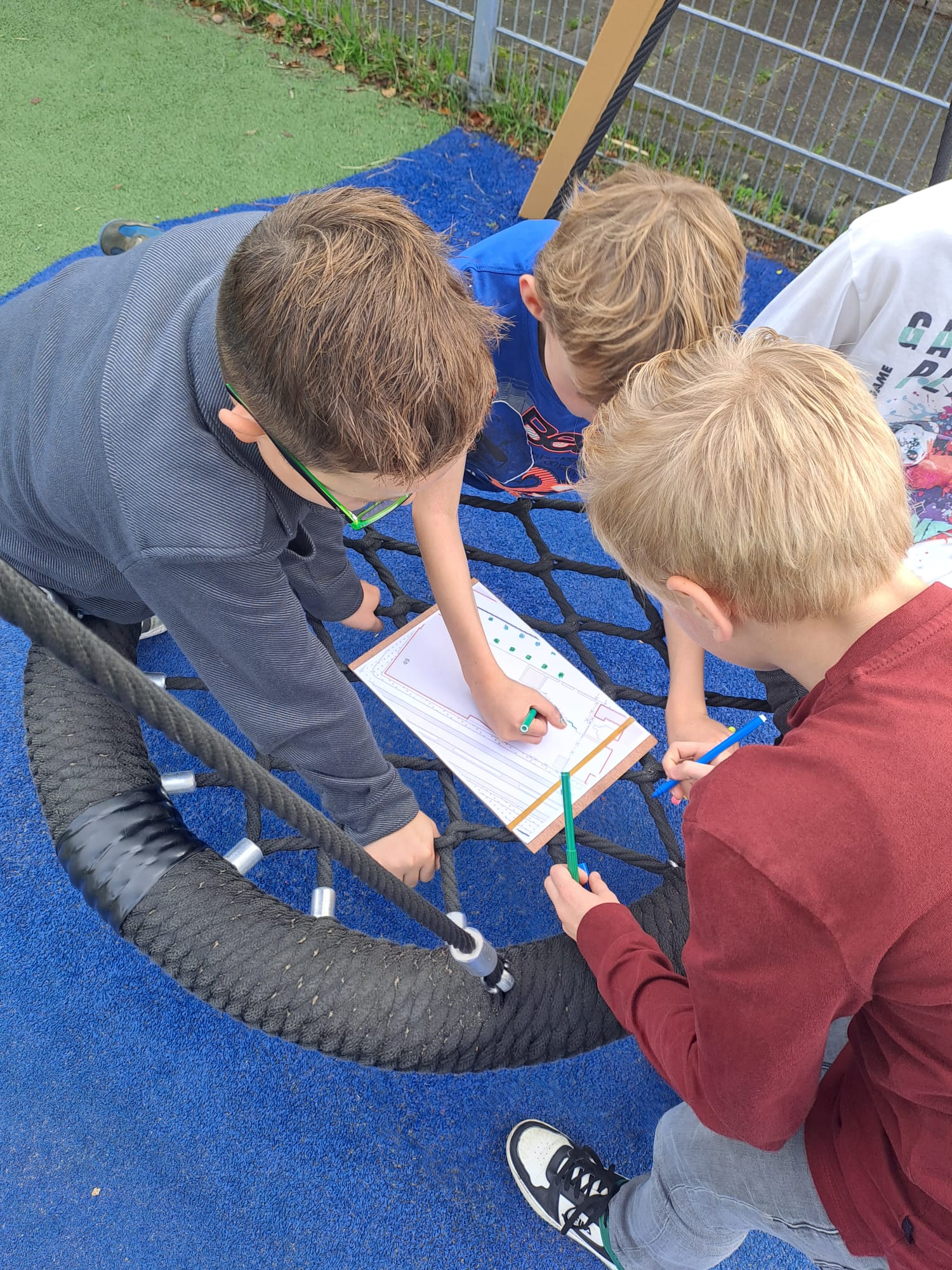 Kinderen tekenen samen op papier in een speeltoestel op een blauwe speelplaats.