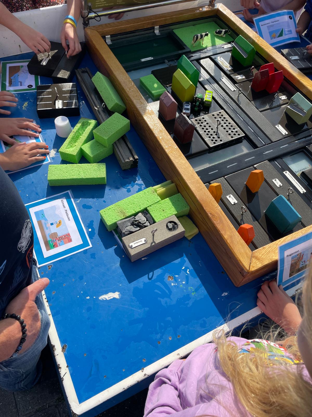 Kinderen spelen met een interactieve maquette van een stad opgebouwd uit blokken en speelgoedauto's.