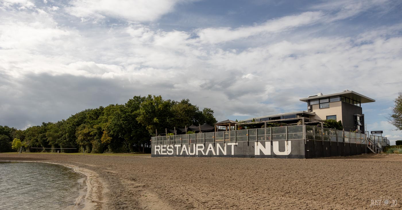 Restaurant aan het strand met omringende bomen en wolkenlucht.