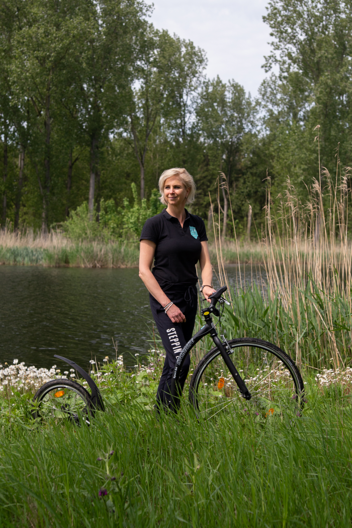 Vrouw met stepfiets in een groen park bij een vijver.