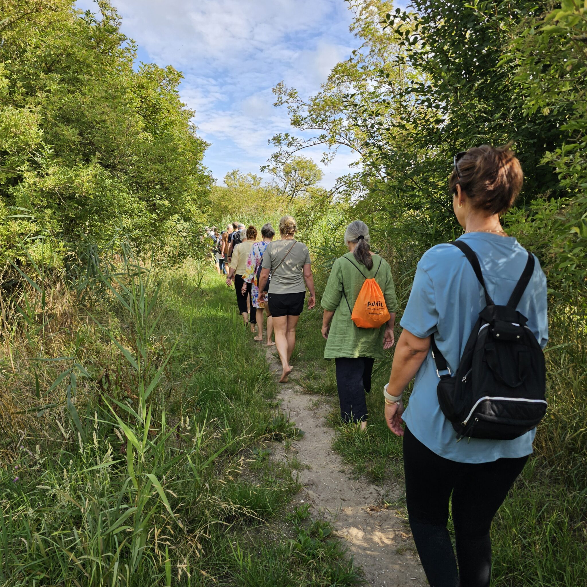 Een groep mensen wandelt op een smal pad door een groen bos, op blote voeten.