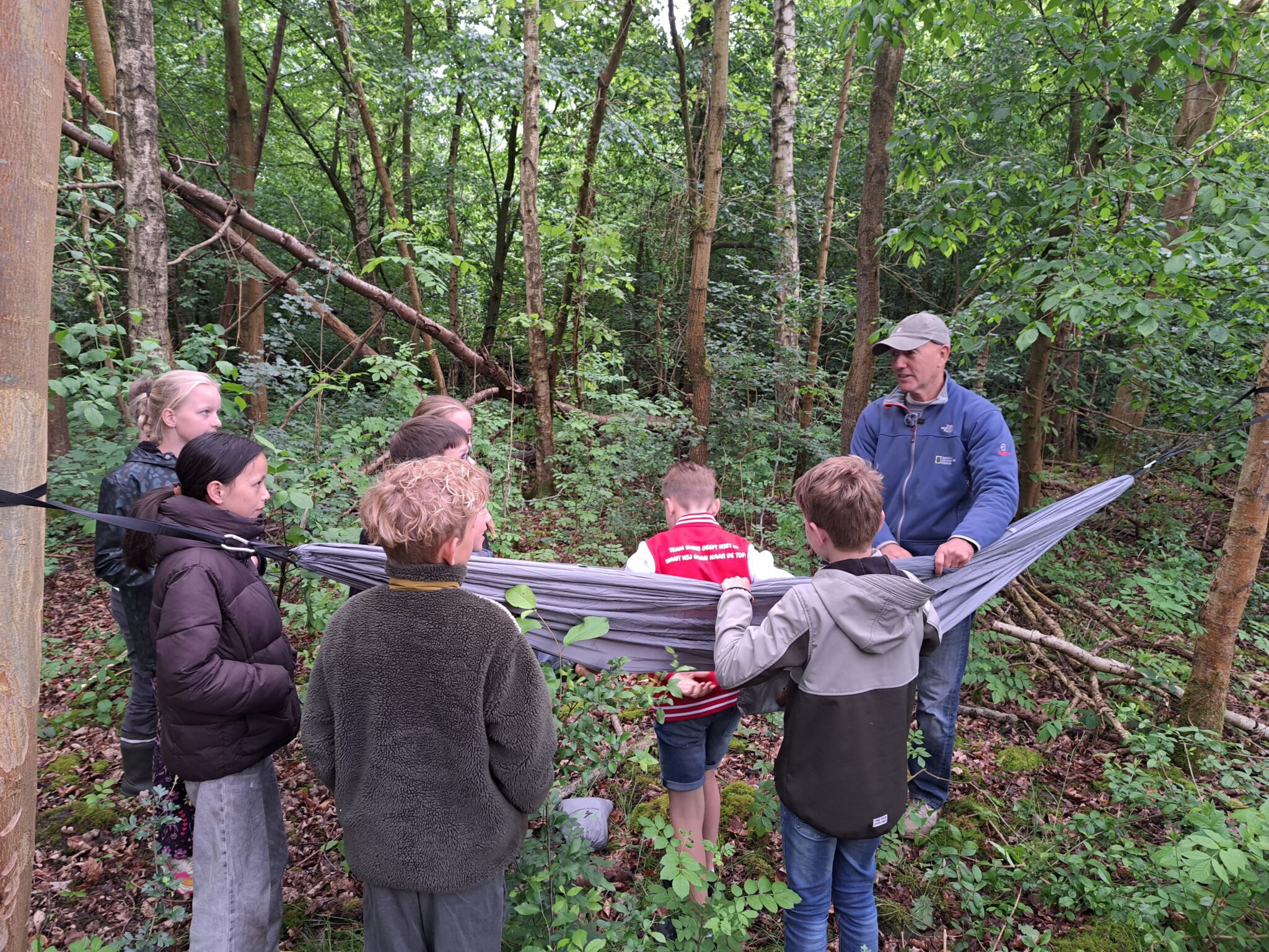 Kinderambassadeurs en expeditieleider Michel Boeijen in een bos rond een hangmat.