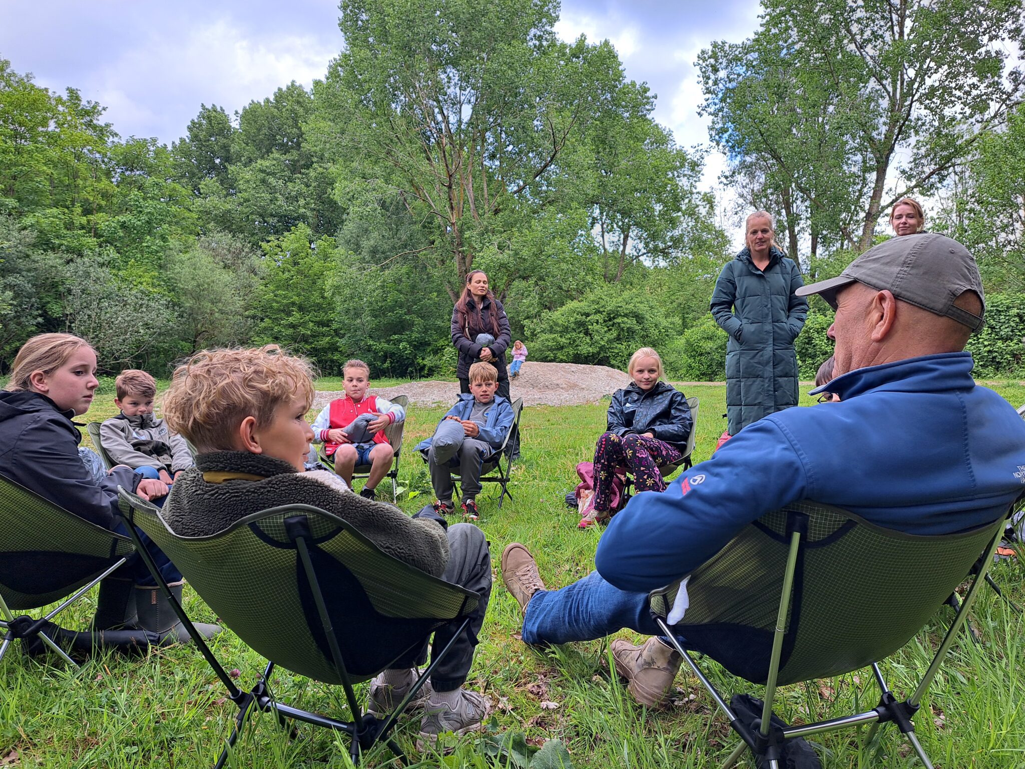 Kinderenambassadeurs en expeditieleider Michel Boeijen zitten in een kring buiten op klapstoelen.
