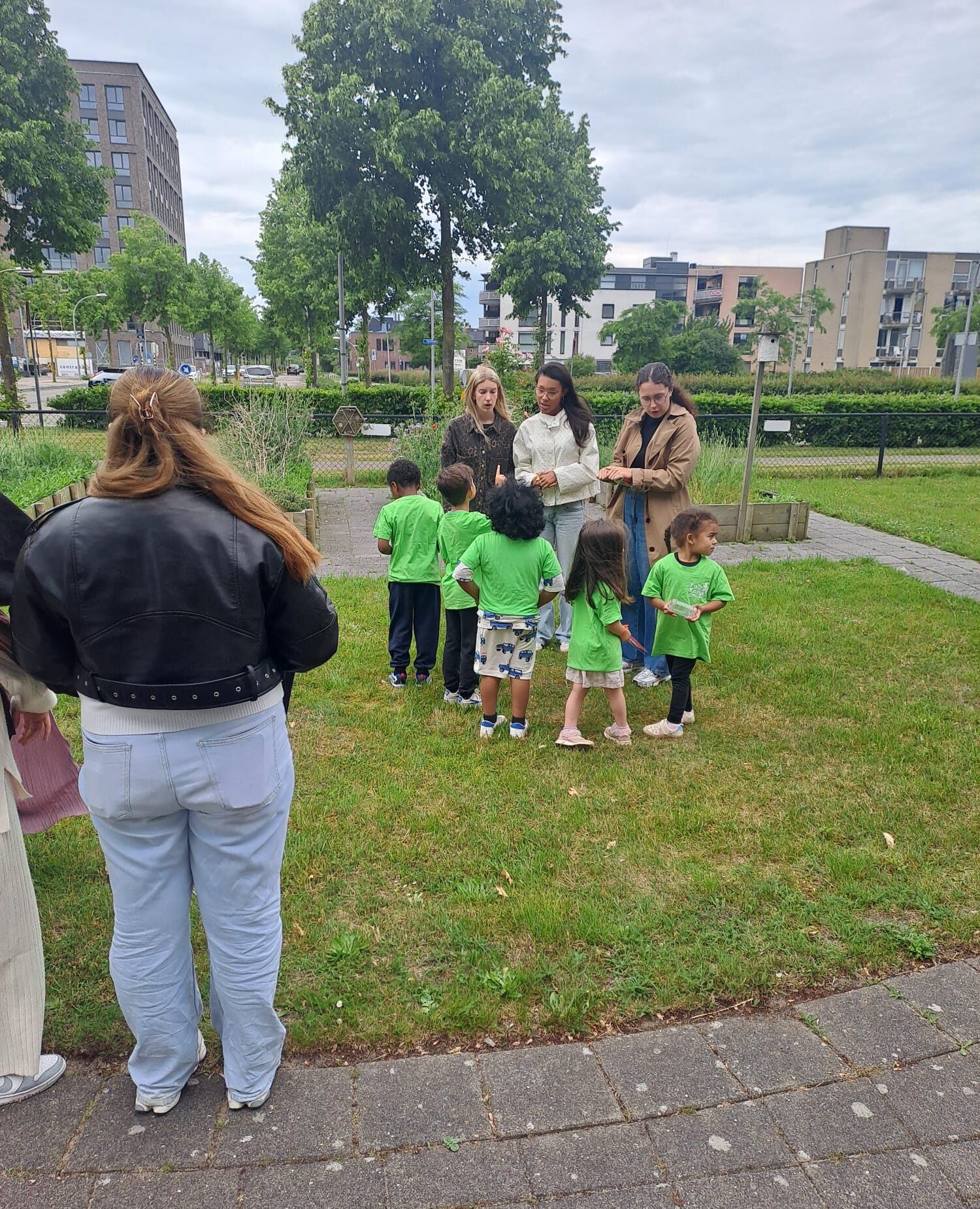Kinderen in groen T-shirt spelen buiten met volwassenen. Stedelijke achtergrond en grasveld.