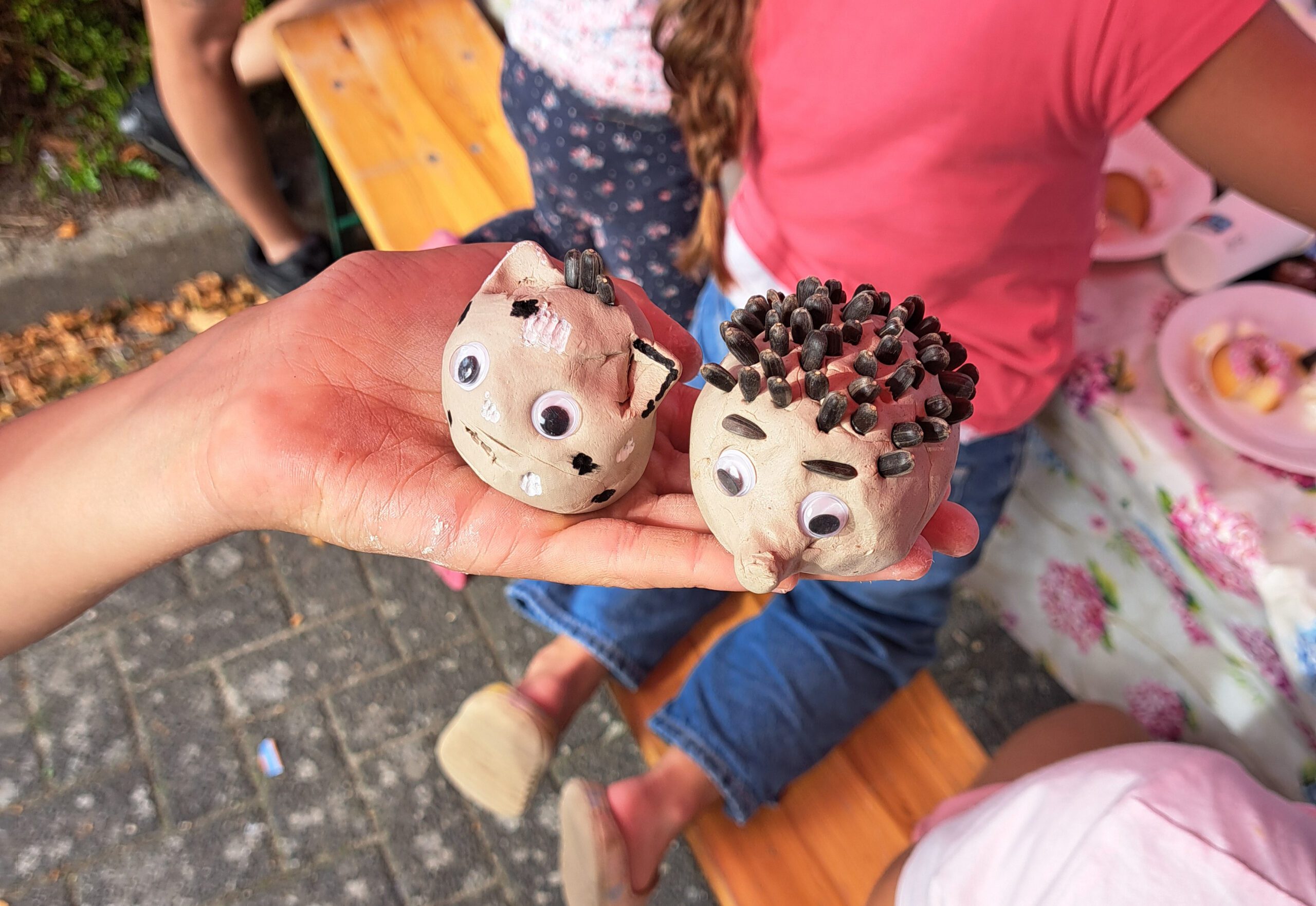 Twee kleibeeldjes van een kat en een egel met wiebeloogjes op een hand tijdens een creatieve activiteit.