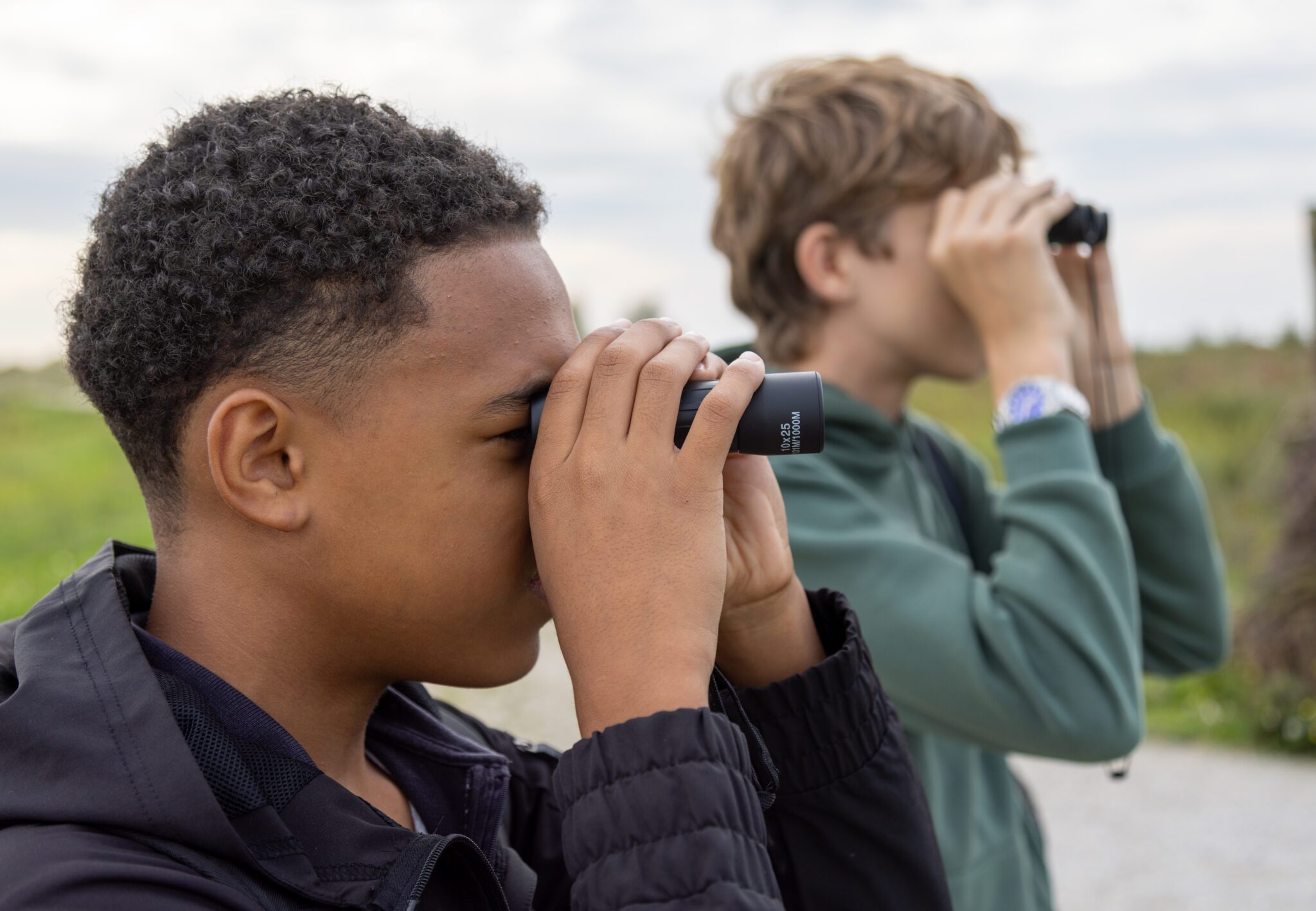 Twee kinderen kijken door verrekijkers in een groene buitenomgeving.