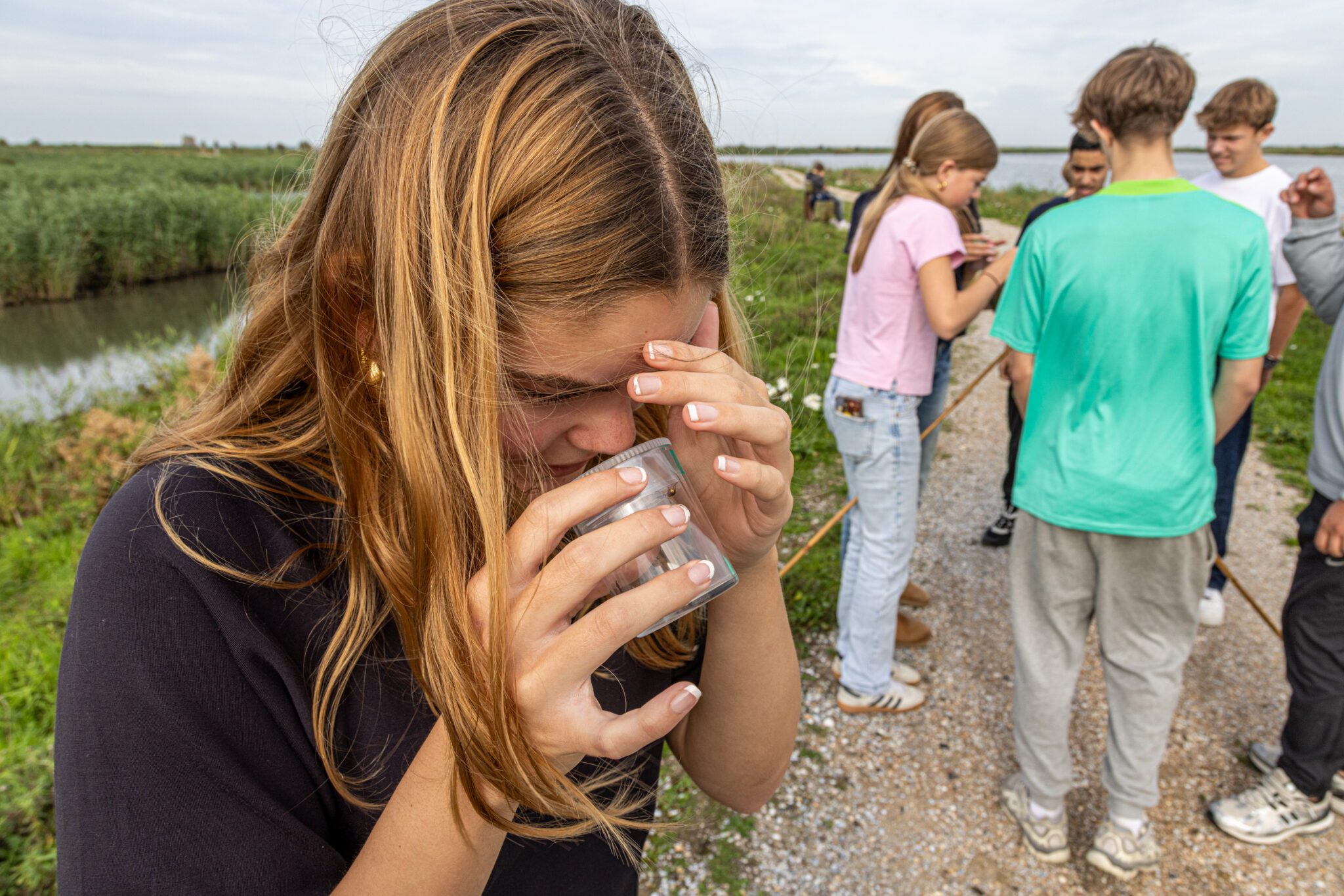 Kind onderzoekt de omgeving met een loep, buiten in de natuur omgeven door andere kinderen.